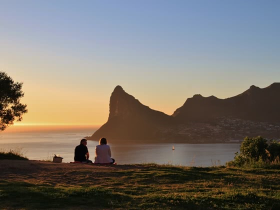 Zwei Menschen blicken bei Sonnenuntergang auf das Meer und die Klippen