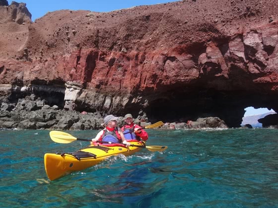 Two people in a kayak on the sea by red cliffs