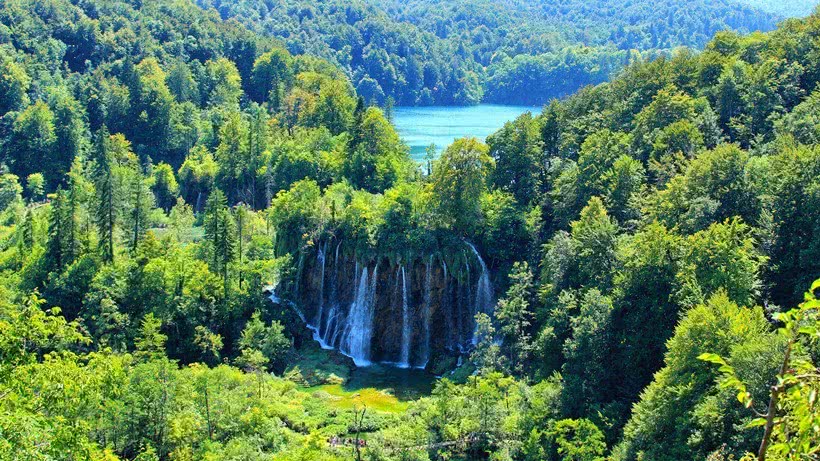 Aerial view of a lake cascading into various waterfalls set in a very lush green forest