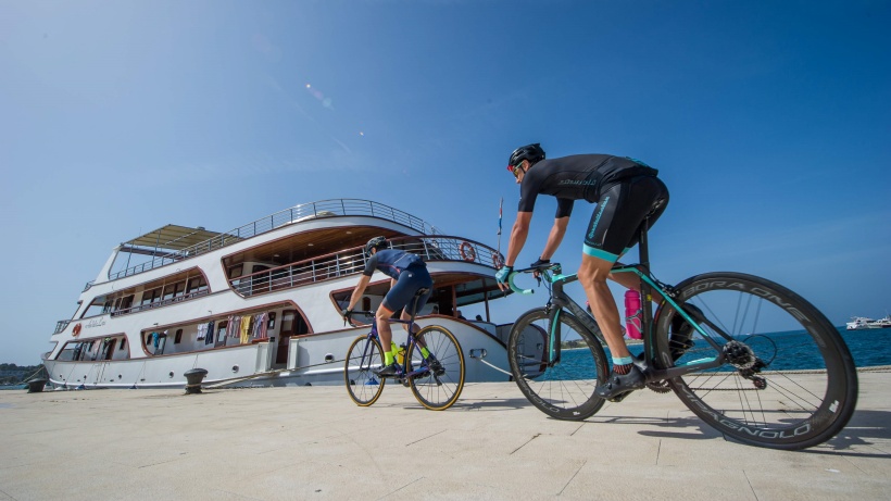 Zwei Rennradfahrer fahren im Hafen auf das Schiff Andela Lora zu