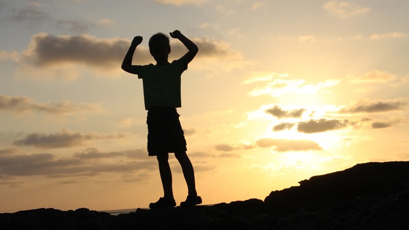 Silhouette of a boy in the evening light with arms raised in victory